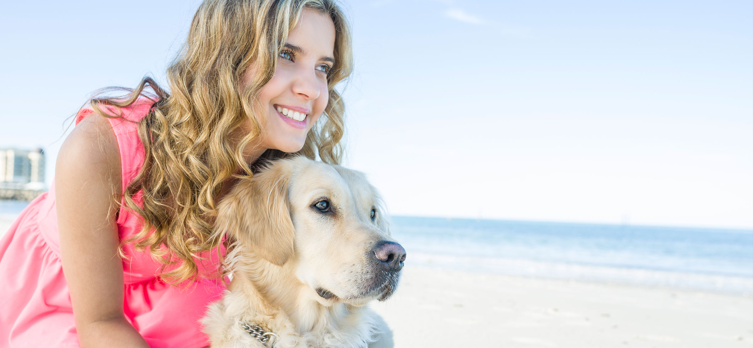 Young woman standing close to a yellow Guide Dog. Beach in the foreground.
