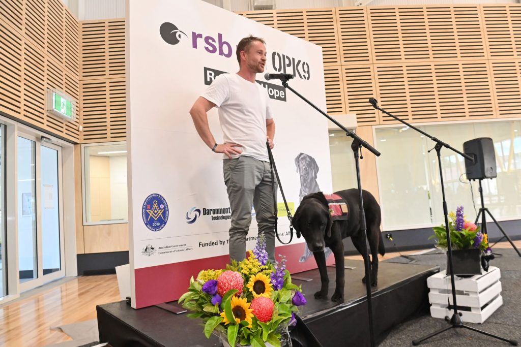 Man with black Assistance Dog on a stage